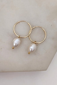 A pair of gold-filled hoop earrings with freshwater pearl drops, displayed on a marble surface.