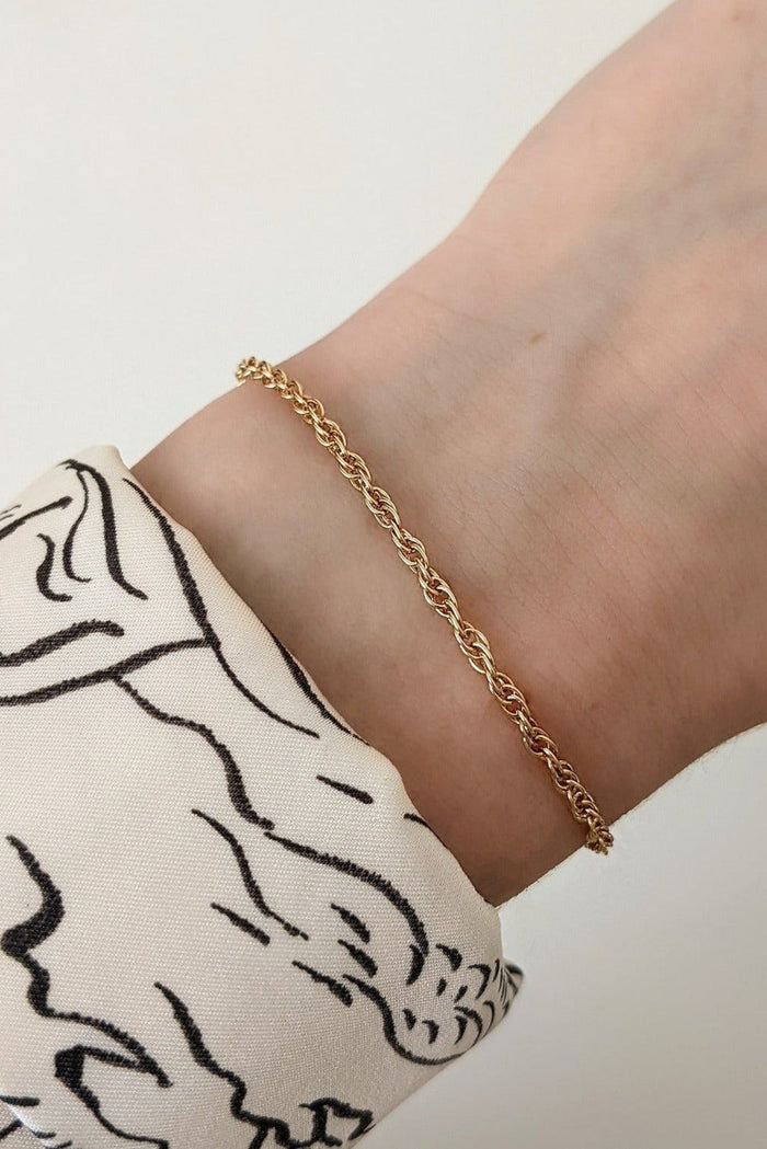 A gold-filled chain bracelet on a person's wrist, featuring a subtle yet intricate rope chain design.